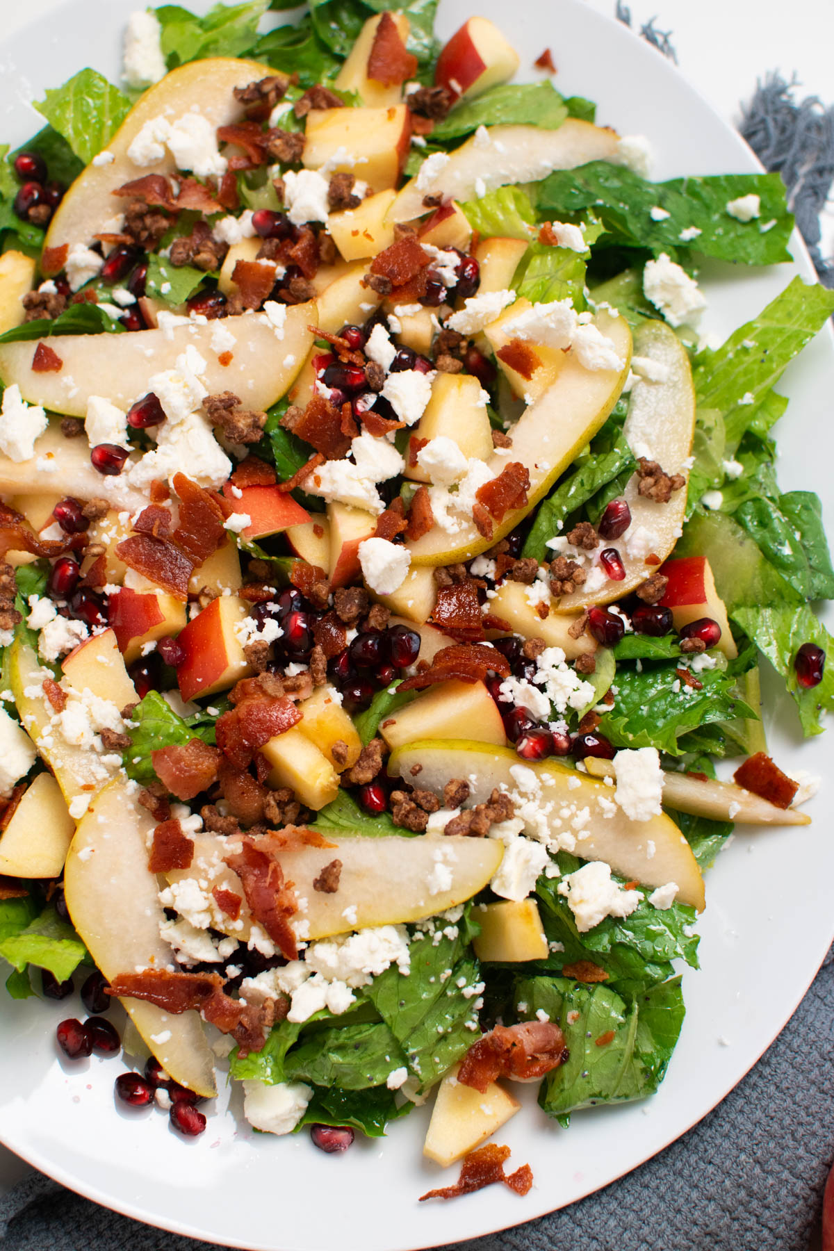 Close up of winter green salad with pears, bacon, and feta on white platter.