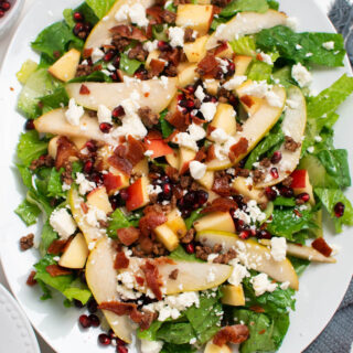 Winter pear salad with bacon, pomegranate seeds, and apples on white platter.