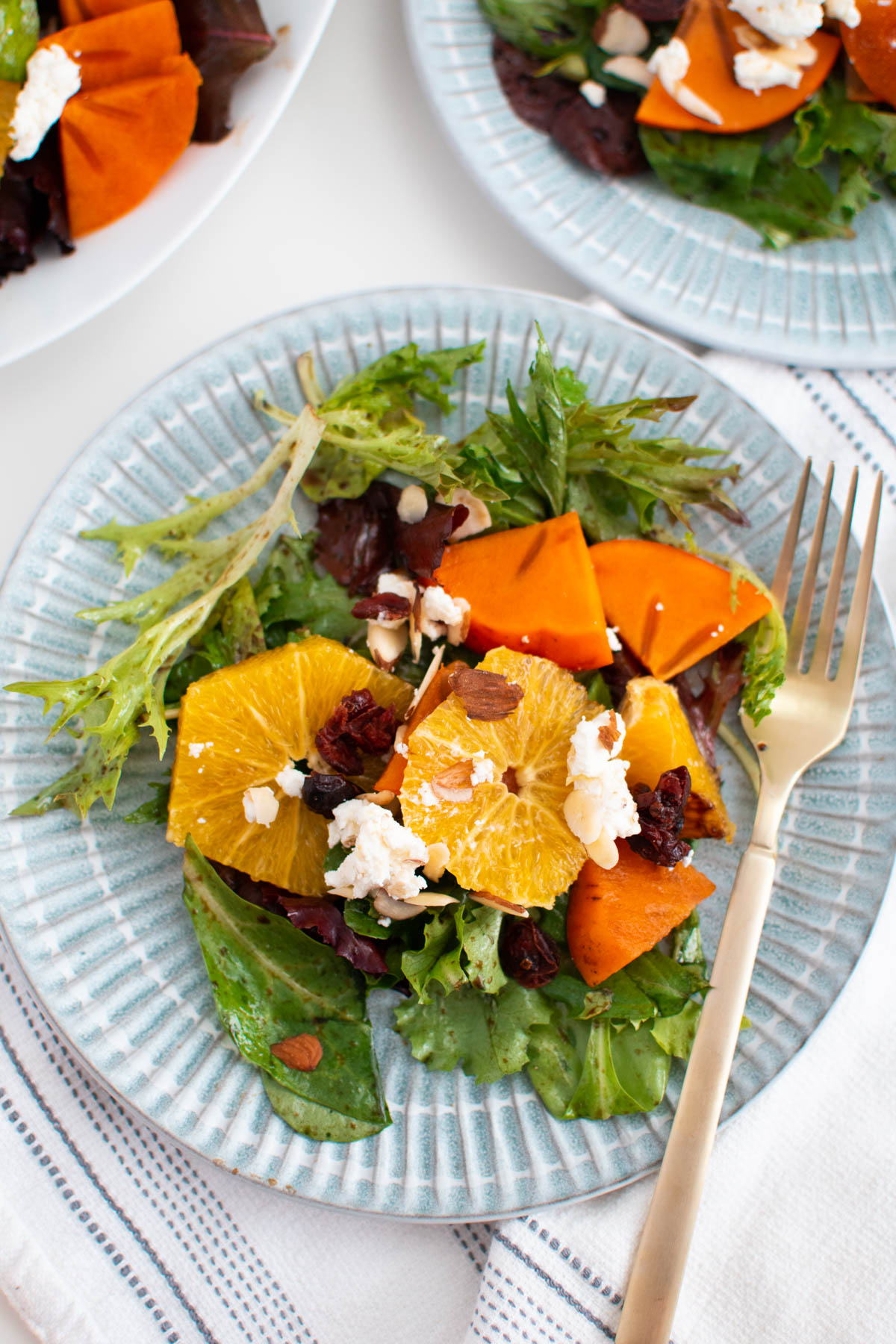 Blue plate with persimmon salad and gold fork.