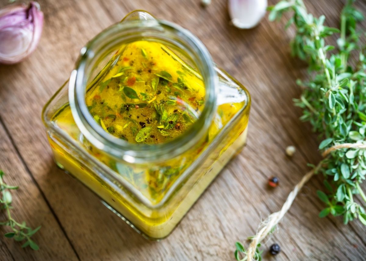 Glass jar filled with vinaigrette dressing with green and red herbs and spices.