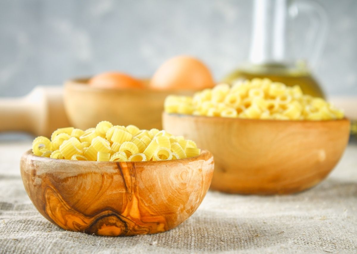 Tubettini pasta in two rustic wooden bowls on table lined with cloth.