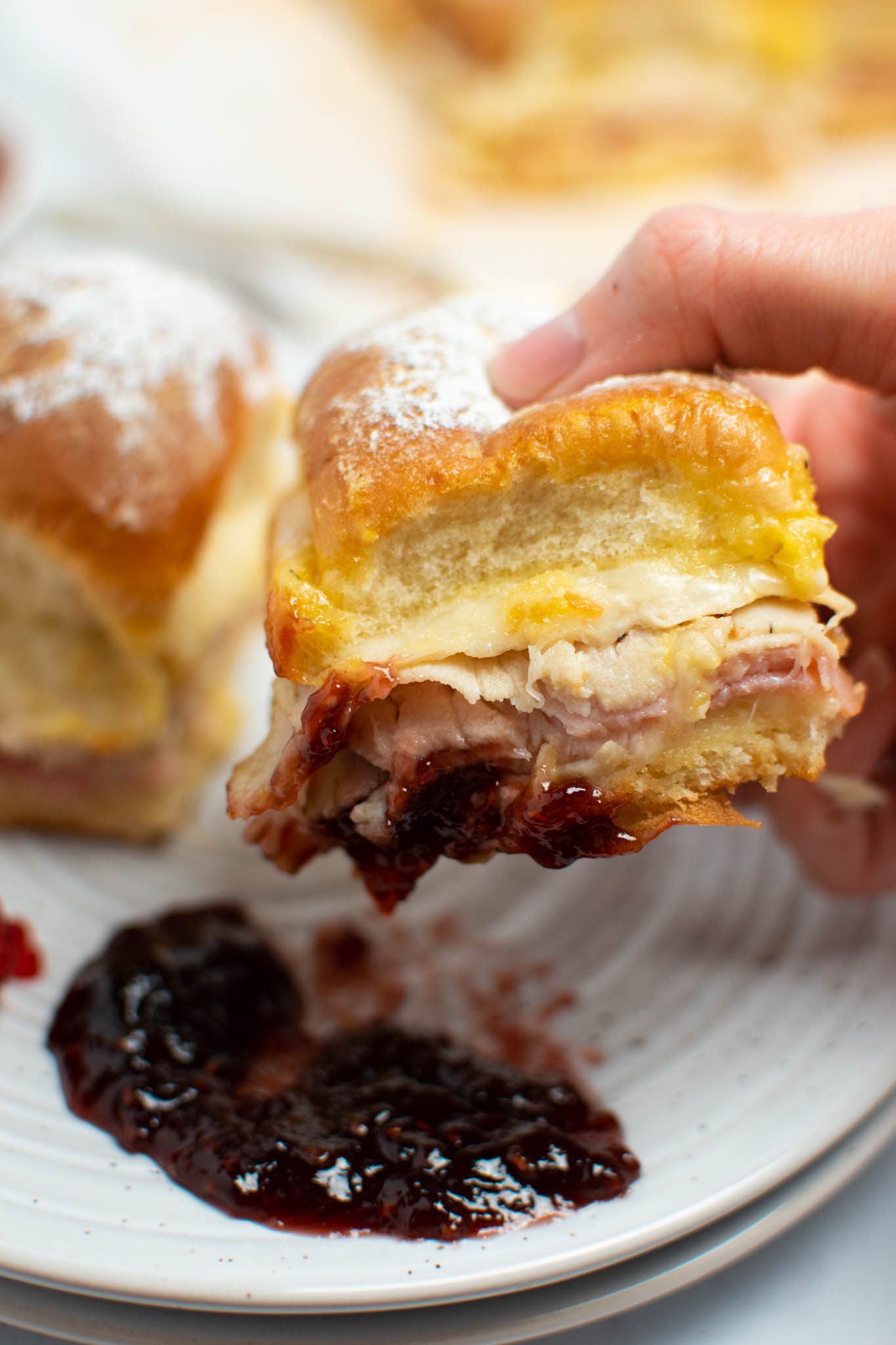Woman holds Monte Cristo slider that's been dunked in raspberry jam.
