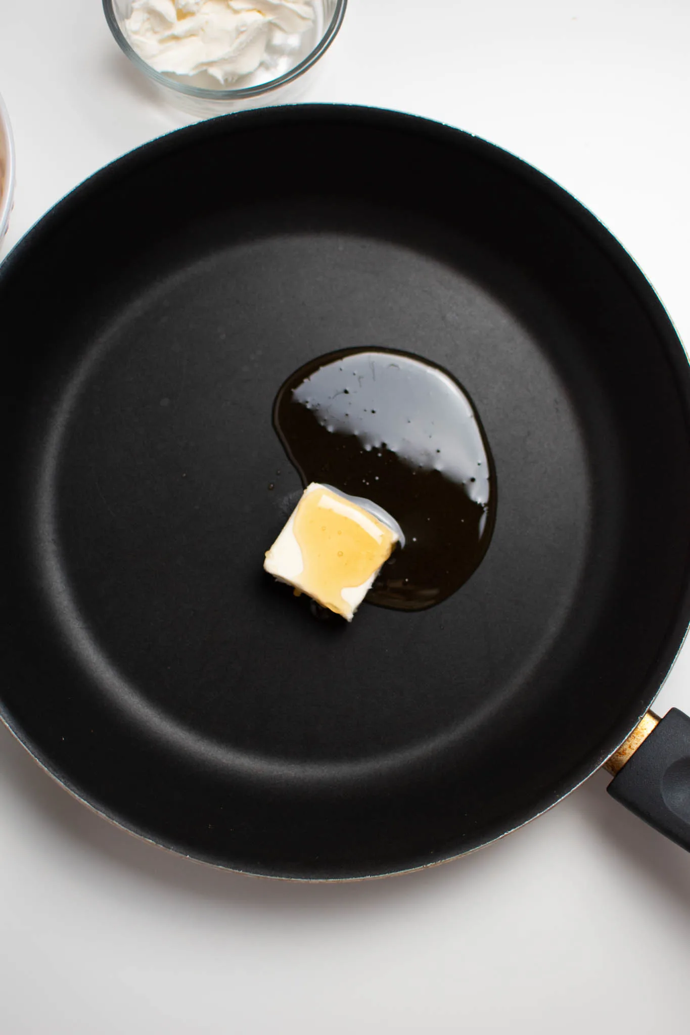 Square of butter and some honey in black frying pan on white table.