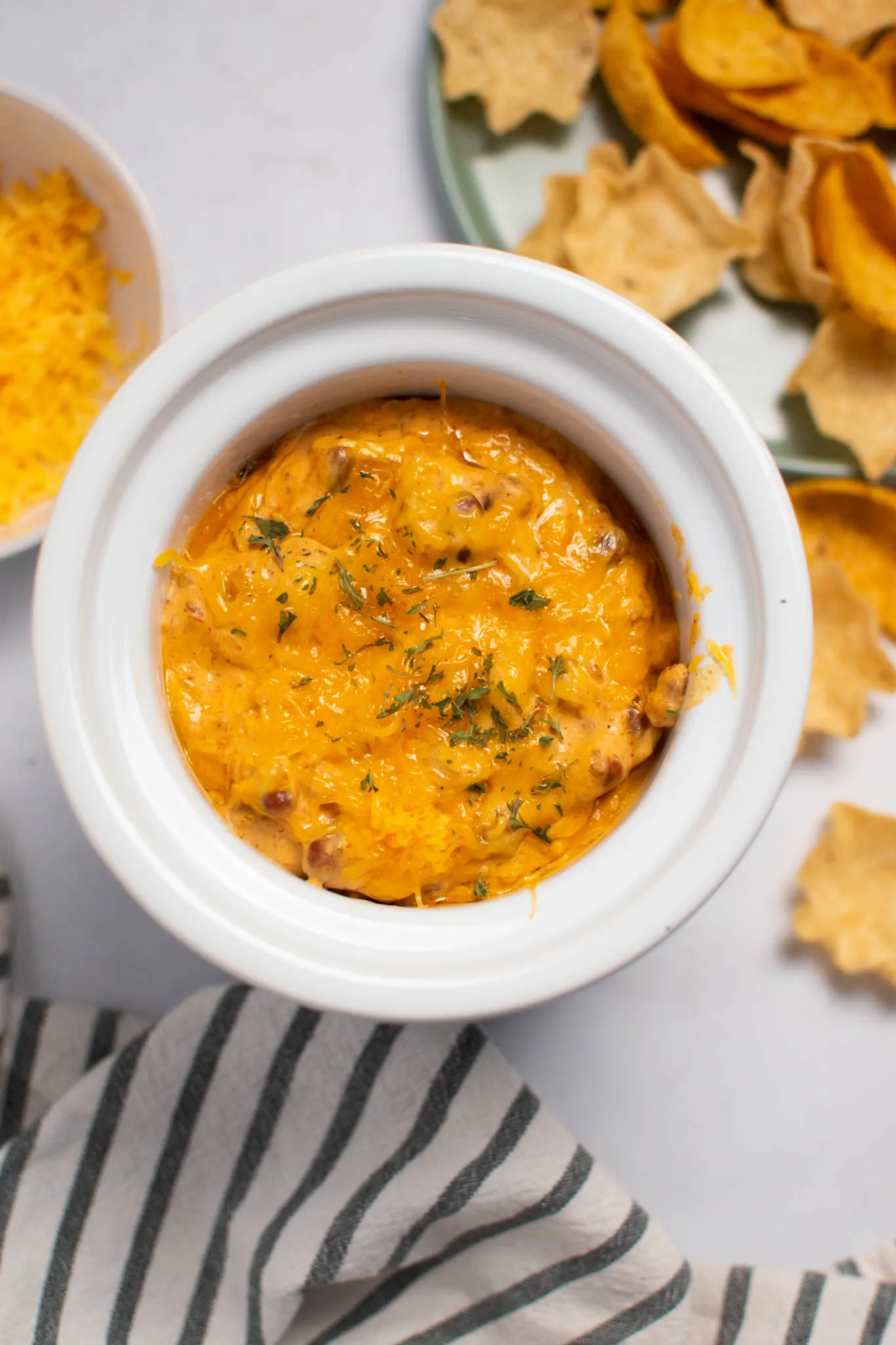 Chili cream cheese dip in small Crock Pot with tortilla chips and striped towel nearby.
