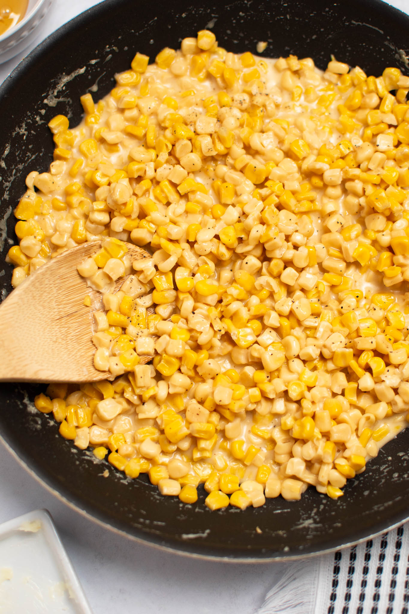 Wooden spoon rests in black frying pan filled with honey butter corn.