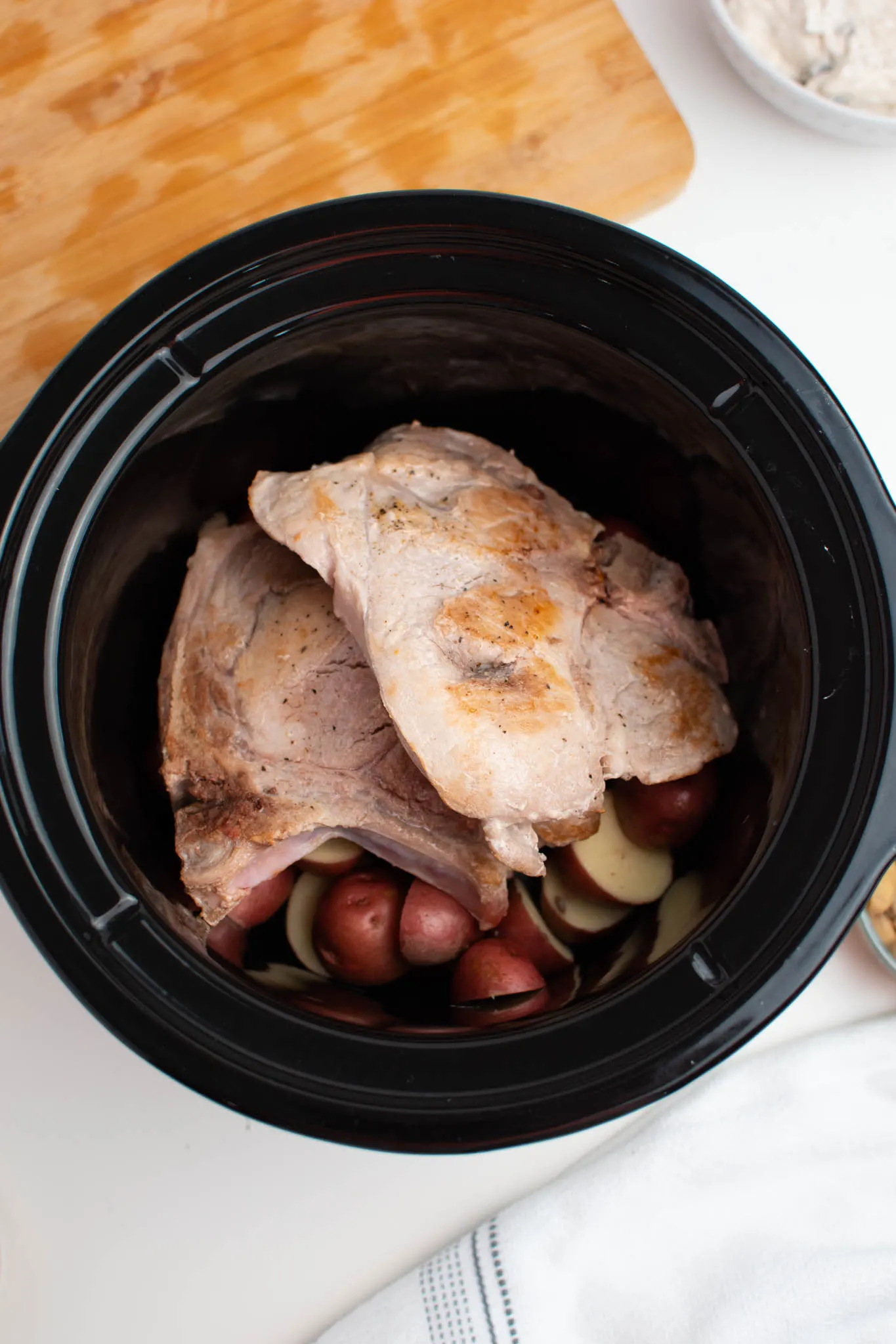 Browned pork chops and raw red potatoes in black Crock Pot insert.