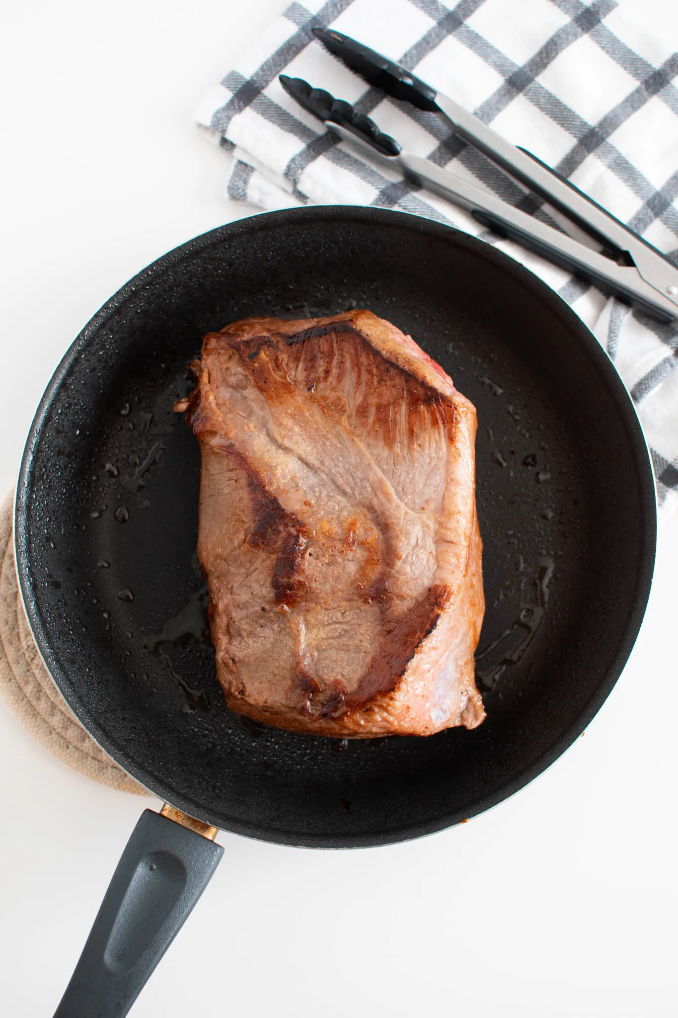 Seared roast in black frying pan on white table.