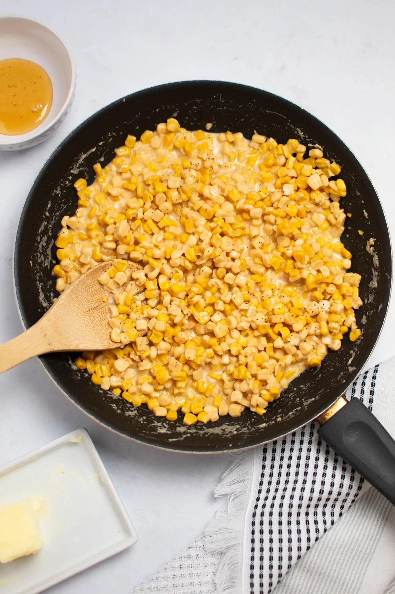 Black frying pan full of skillet fried corn with bowl of honey and butter dish nearby.