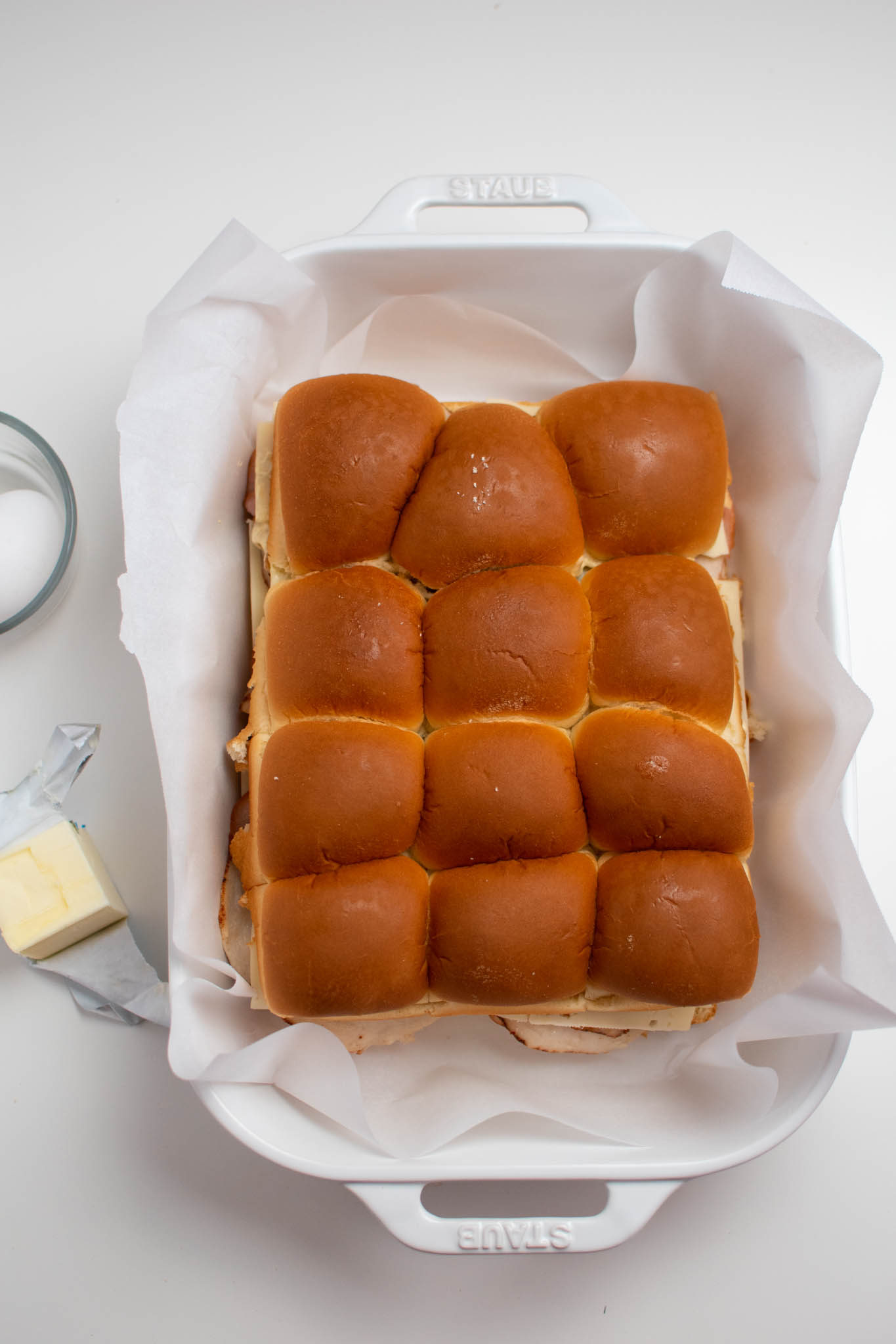 Unbaked sliders in white baking dish with parchment paper.