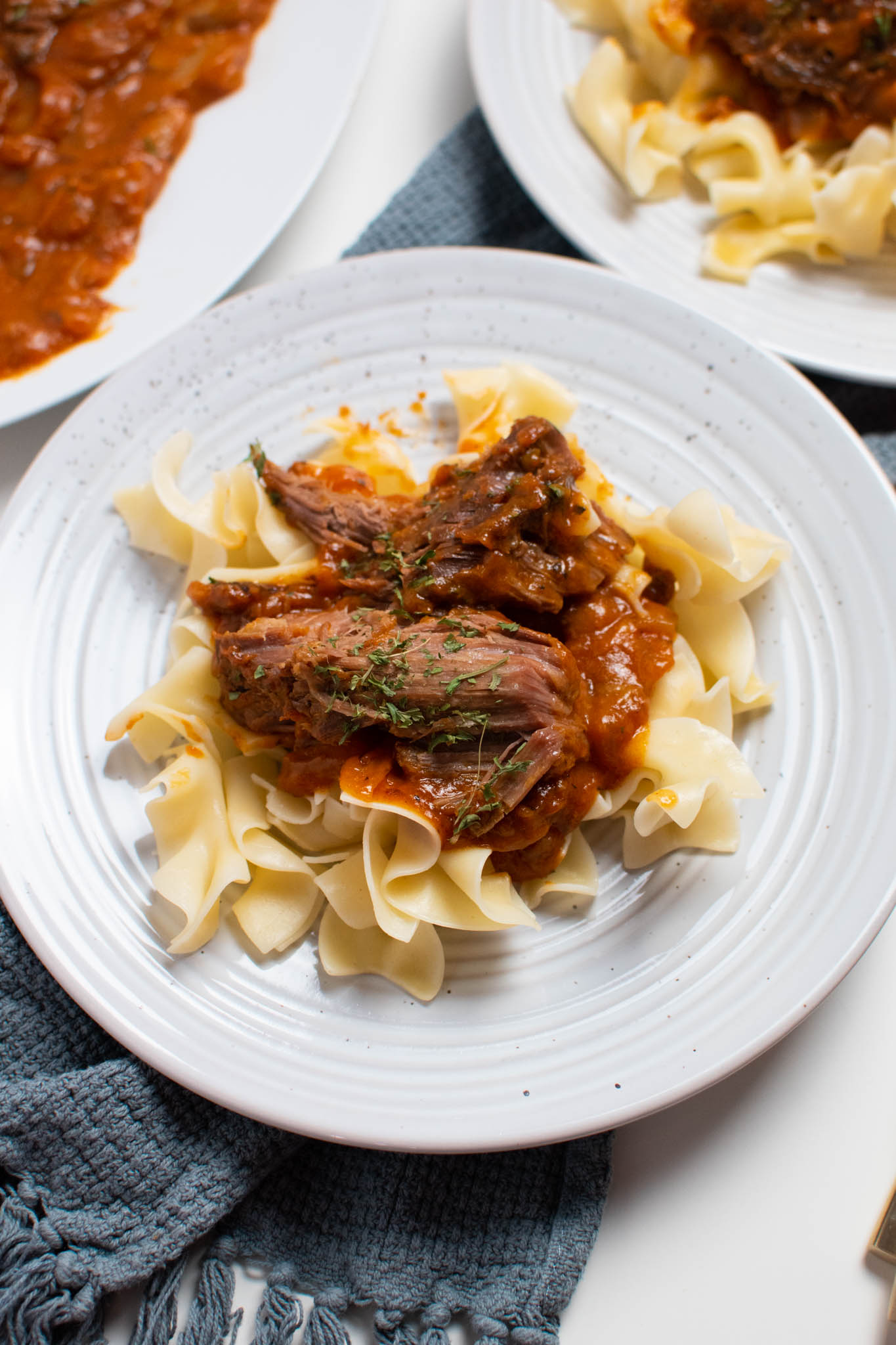 Italian pot roast and sauce over egg noodles on white plate.