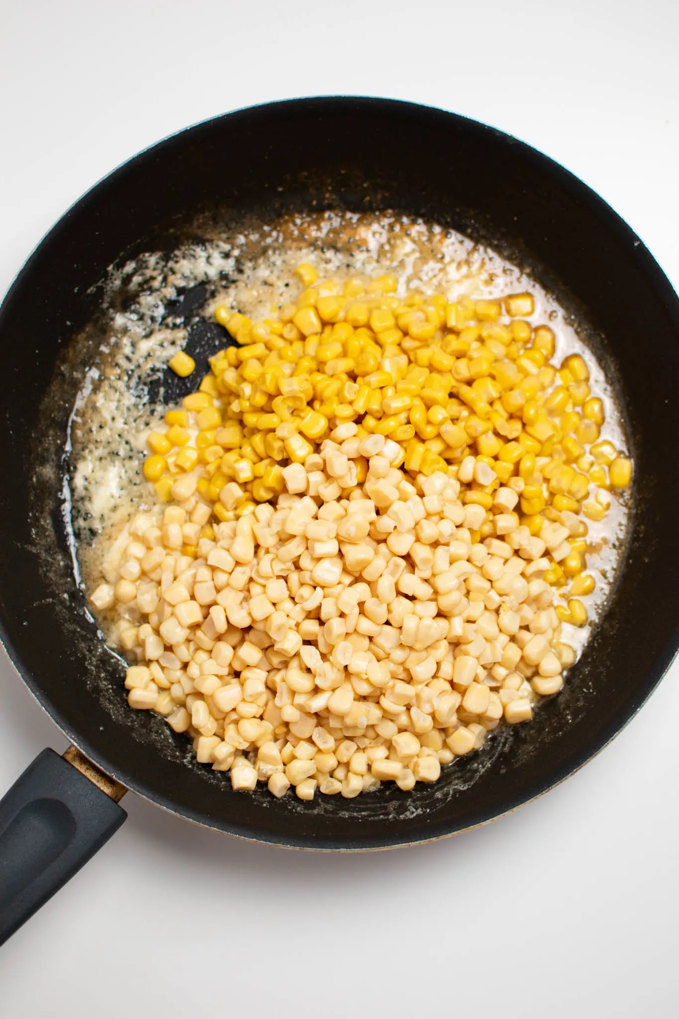 Piles of yellow and white corn kernels in black frying pan.