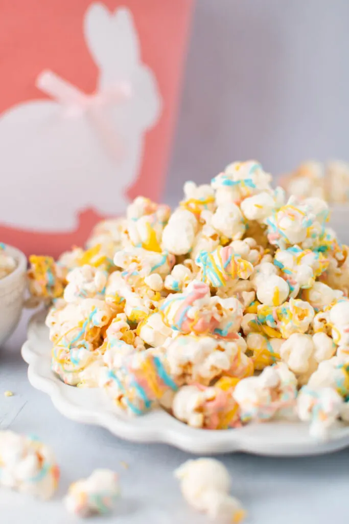 Large pile of bunny bait popcorn on white platter with Easter bunny basket in background.