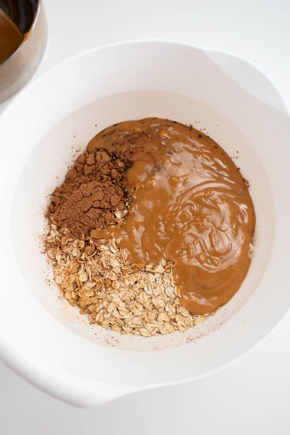 Cocoa, oats, and melted peanut butter in large white mixing bowl.