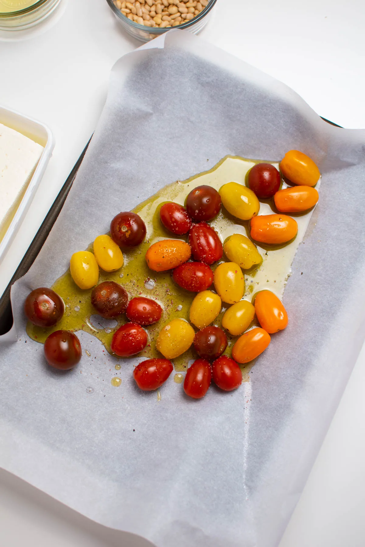 Several colored cherry tomatoes and olive oil on a parchment lined baking sheet.