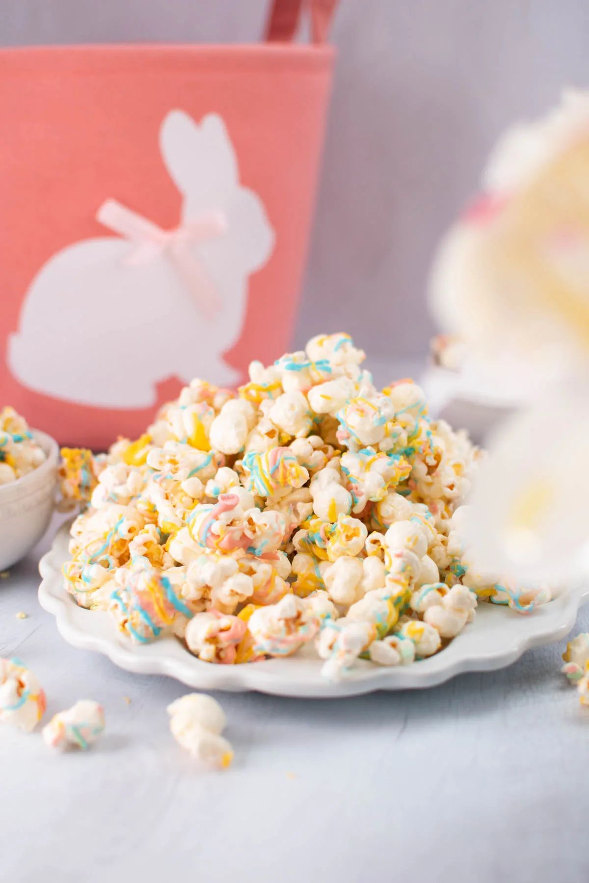 Large pile of easter popcorn on white plate, with pink bunny Easter basket in background.