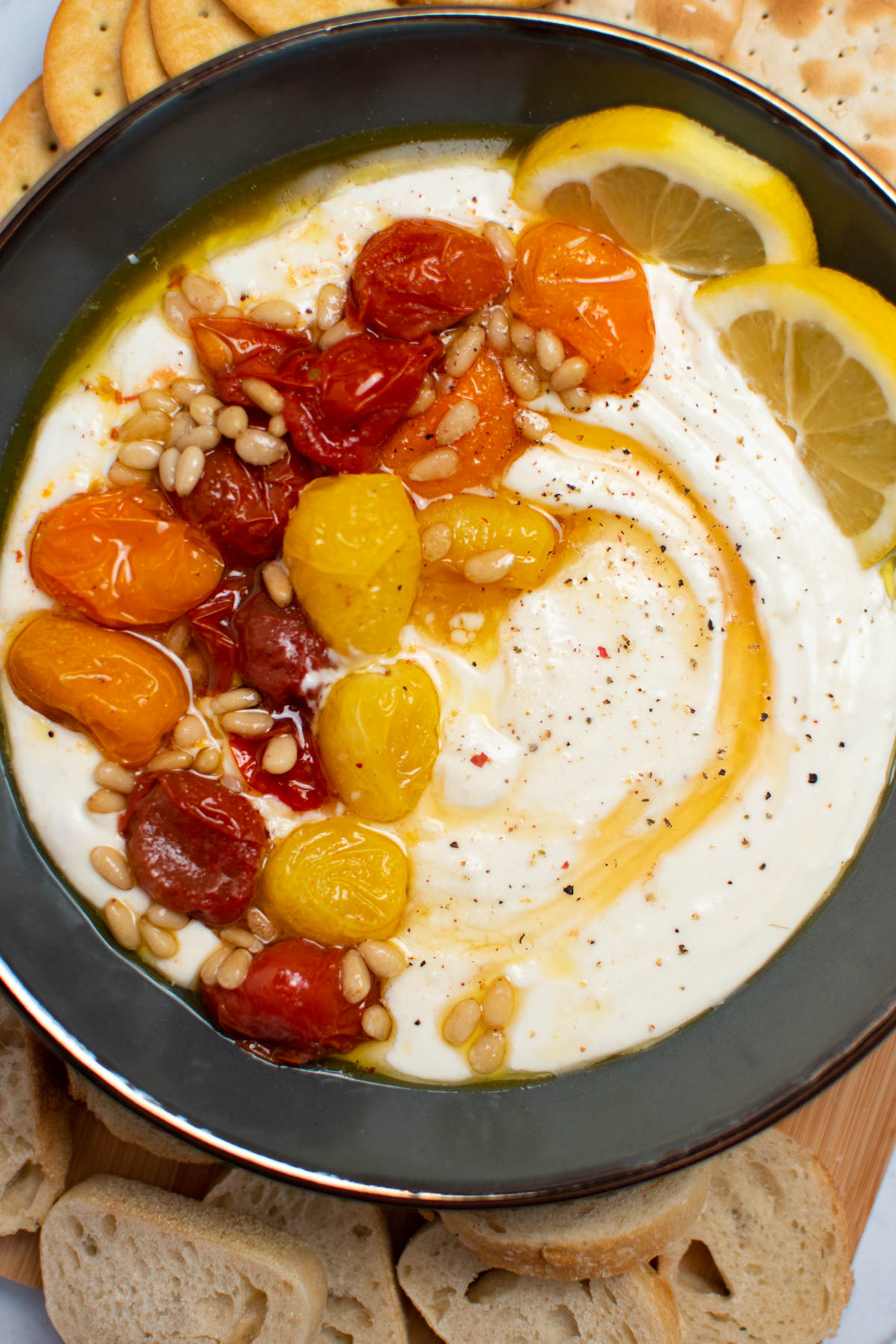 Gray bowl filled with feta dip, roasted tomatoes, pine nuts, honey, and lemon slices.