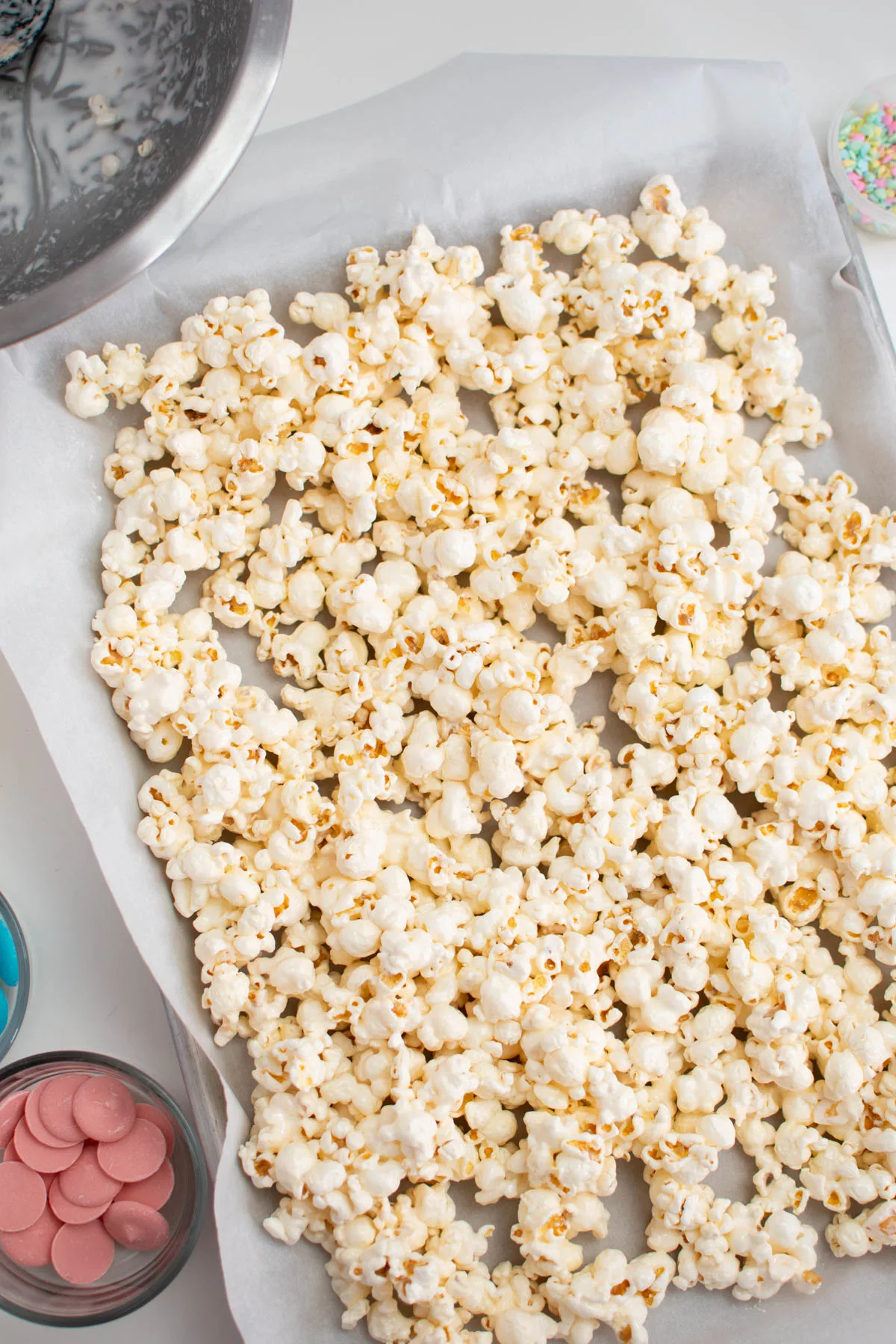 Marshmallow covered popcorn in one layer on parchment covered sheet pan.
