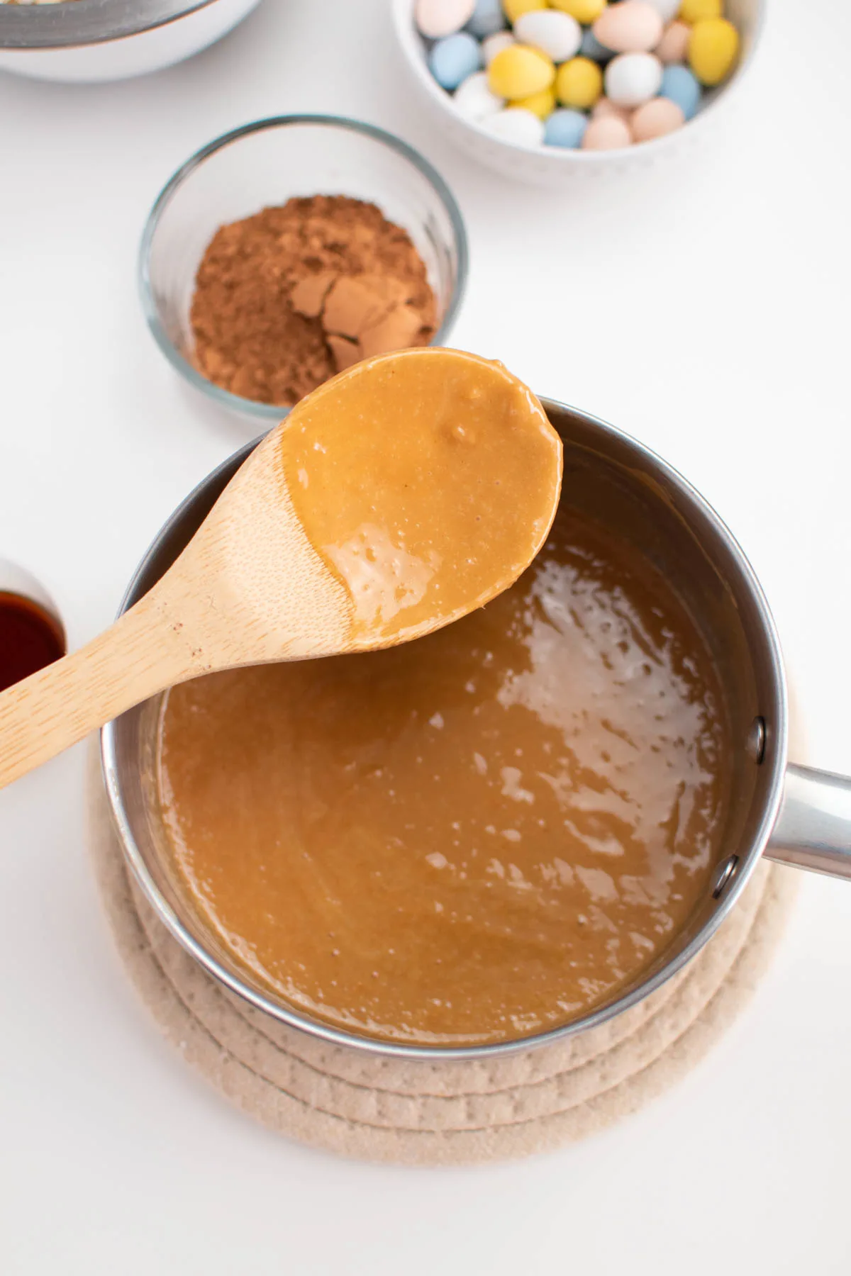 Wooden spoon with melted peanut butter resting over saucepan full of peanut butter mixture.