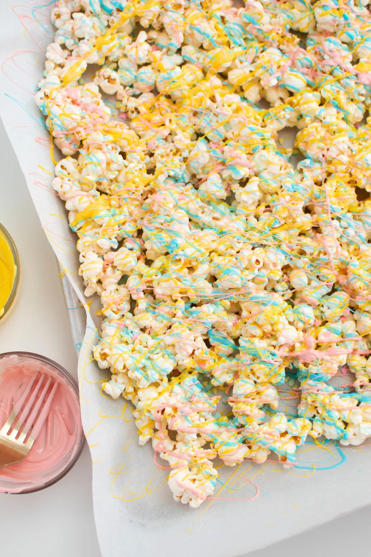 Popcorn drizzled with yellow, pink, and blue chocolate on parchment lined pan.