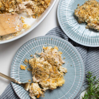 Two blue plates with poppy seed chicken casserole on them next to baking dish of casserole.