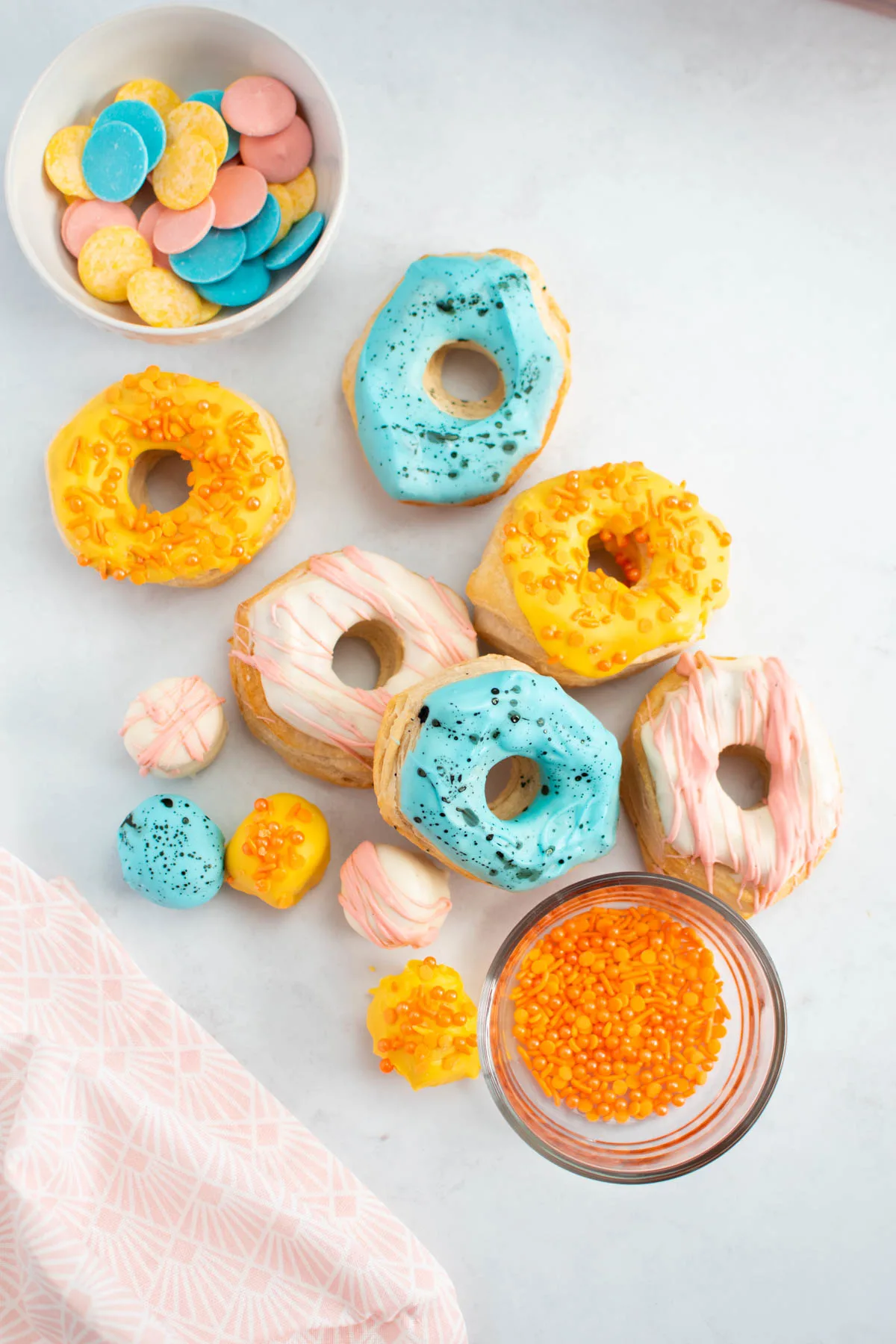 Several air fryer biscuit donuts arranged on table top with bowls of sprinkles and chocolates nearby.