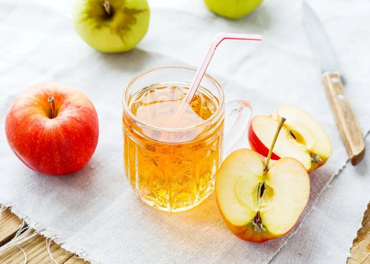 Glass of apple juice with straw surrounded by sliced and whole apples.