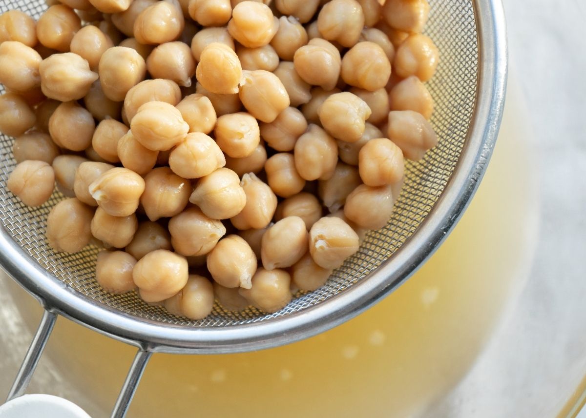 Chickpeas in a strainer with aquafaba liquid draining into glass mixing bowl.