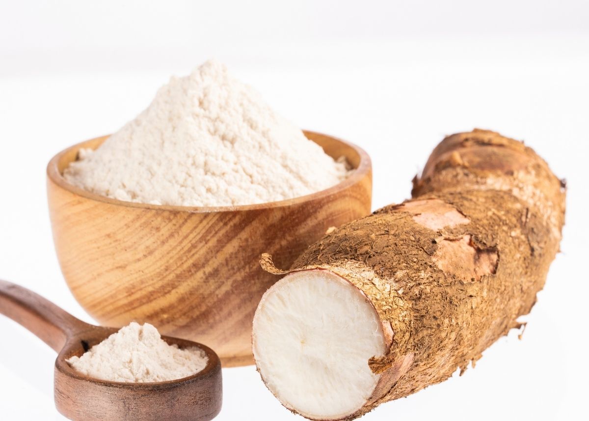 Arrowroot next to large wooden bowl filled with arrowroot powder on white background.
