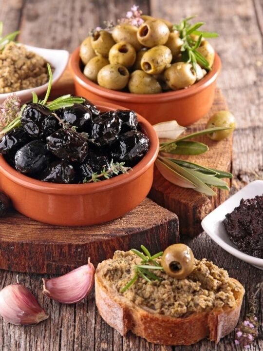 Several bowls of various sizes and colors filled with olives and olive tapenade.