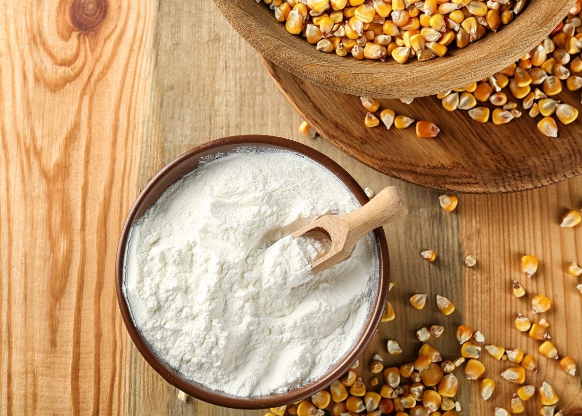 Large bowl of white cornstarch with wooden scoop next to bowl of corn kernels.
