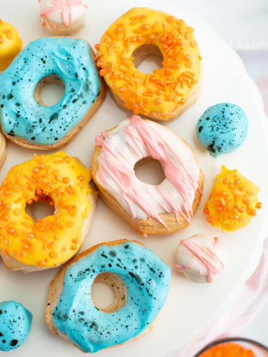 Several Easter decorated air fryer biscuit donuts and donut holes on white cake stand.