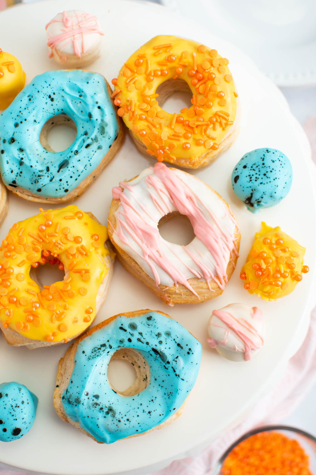Several Easter decorated air fryer biscuit donuts and donut holes on white cake stand.