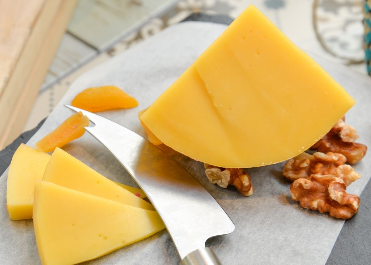 Edam cheese wedge and slices on cutting board with nuts and knife.
