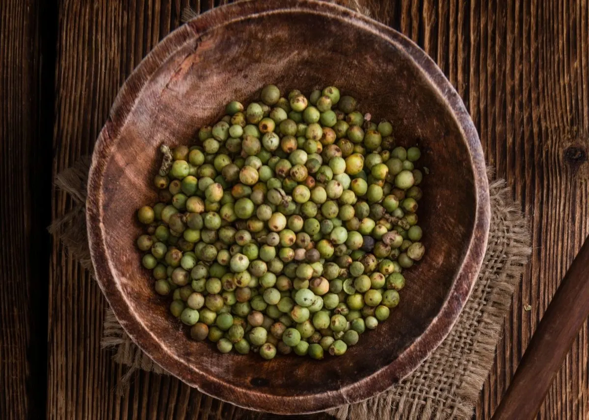 Large wooden bowl filled with green peppercorns on a rustic wooden table.