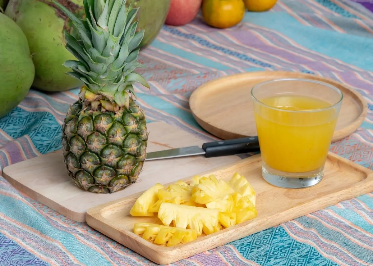 Homemade pineapple juice next to sliced pineapple, a knife, and whole pineapple.
