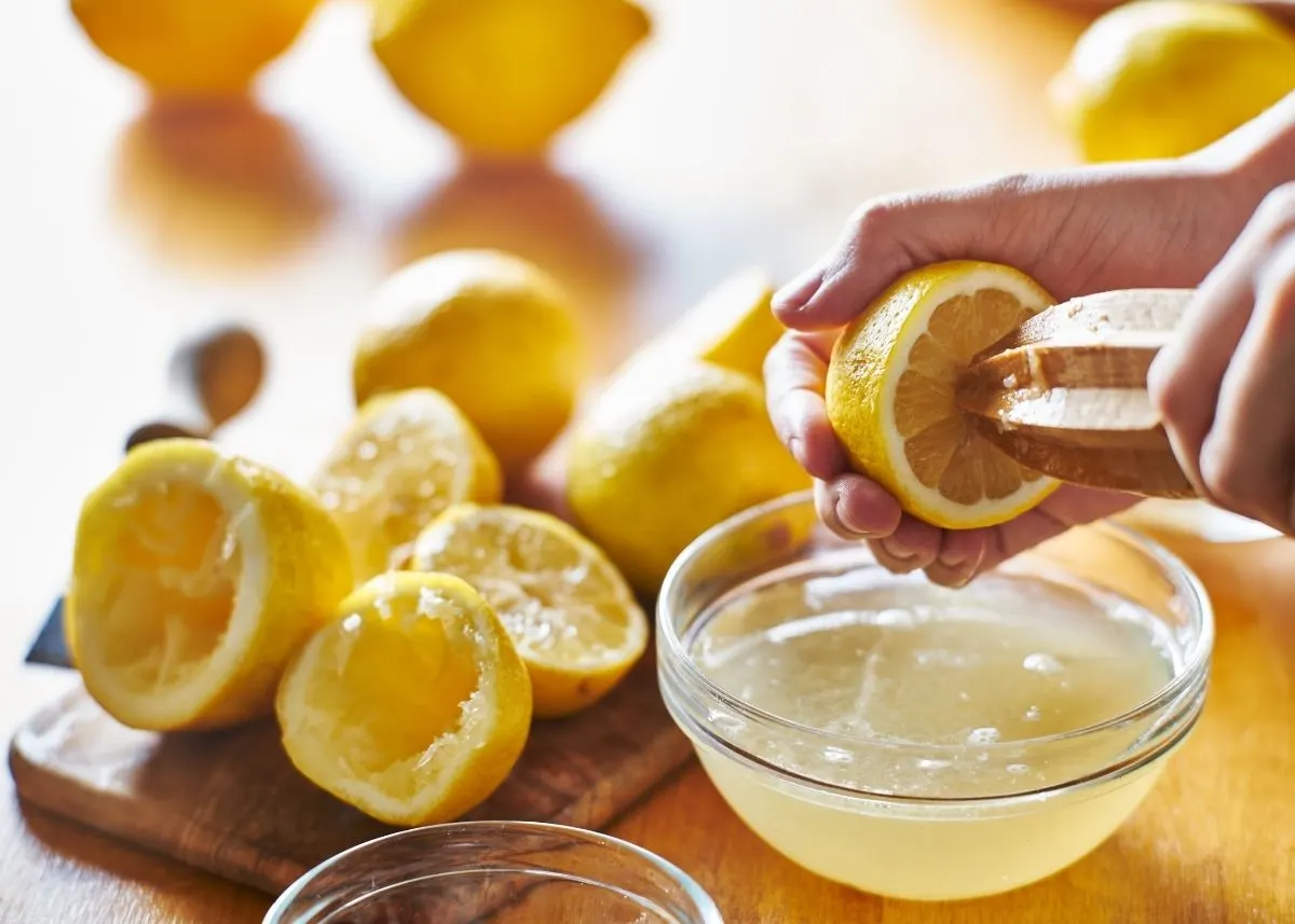 Juiced lemons on a wooden cutting board and woman squeezing lemon juice into bowl.