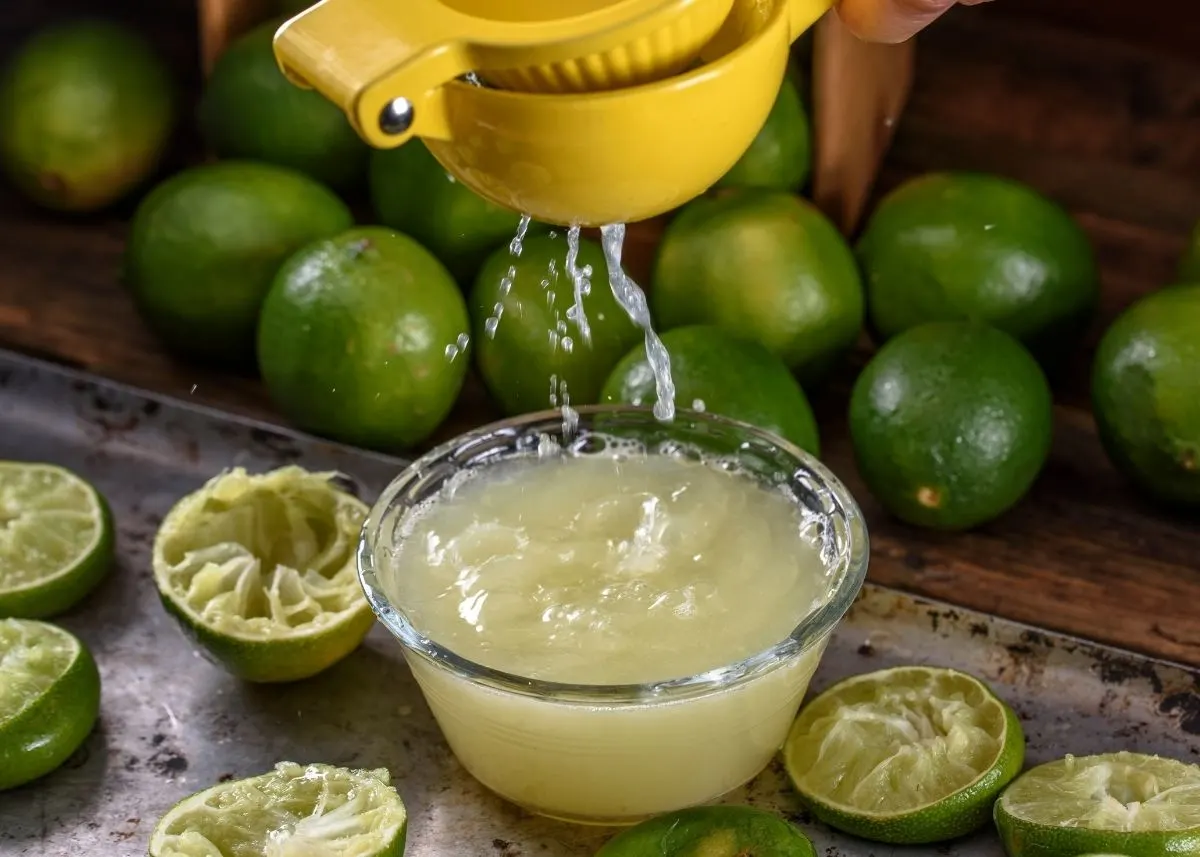 Several fresh limes and lime juice is squeezed into a glass bowl.