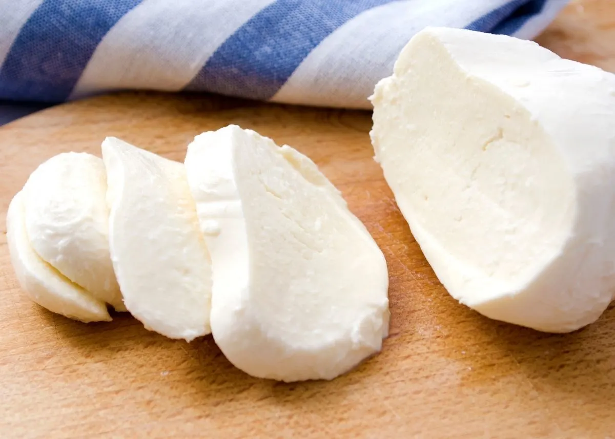 Several slices of mozzarella cheese on a wooden kitchen table with blue and white towel.