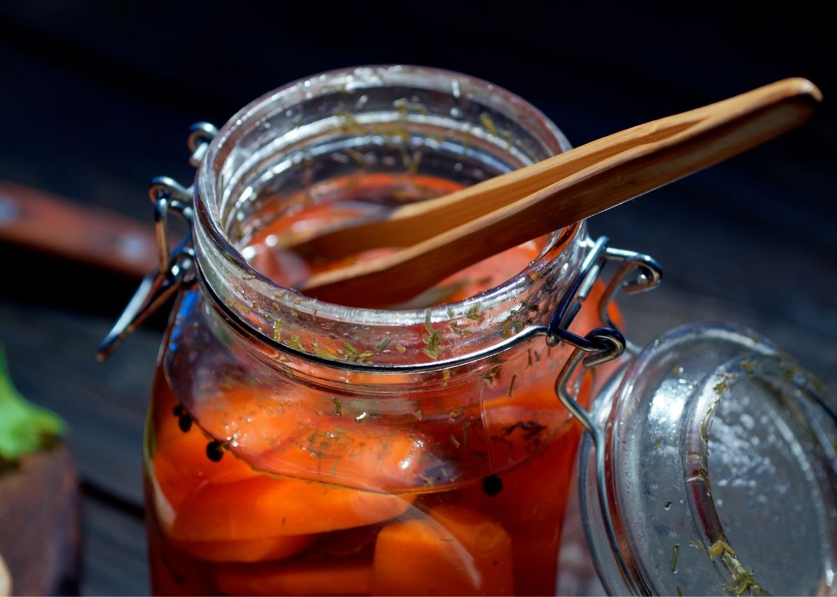 Clear glass mason jar filled with bright orange pickled carrots with wooden spoon.
