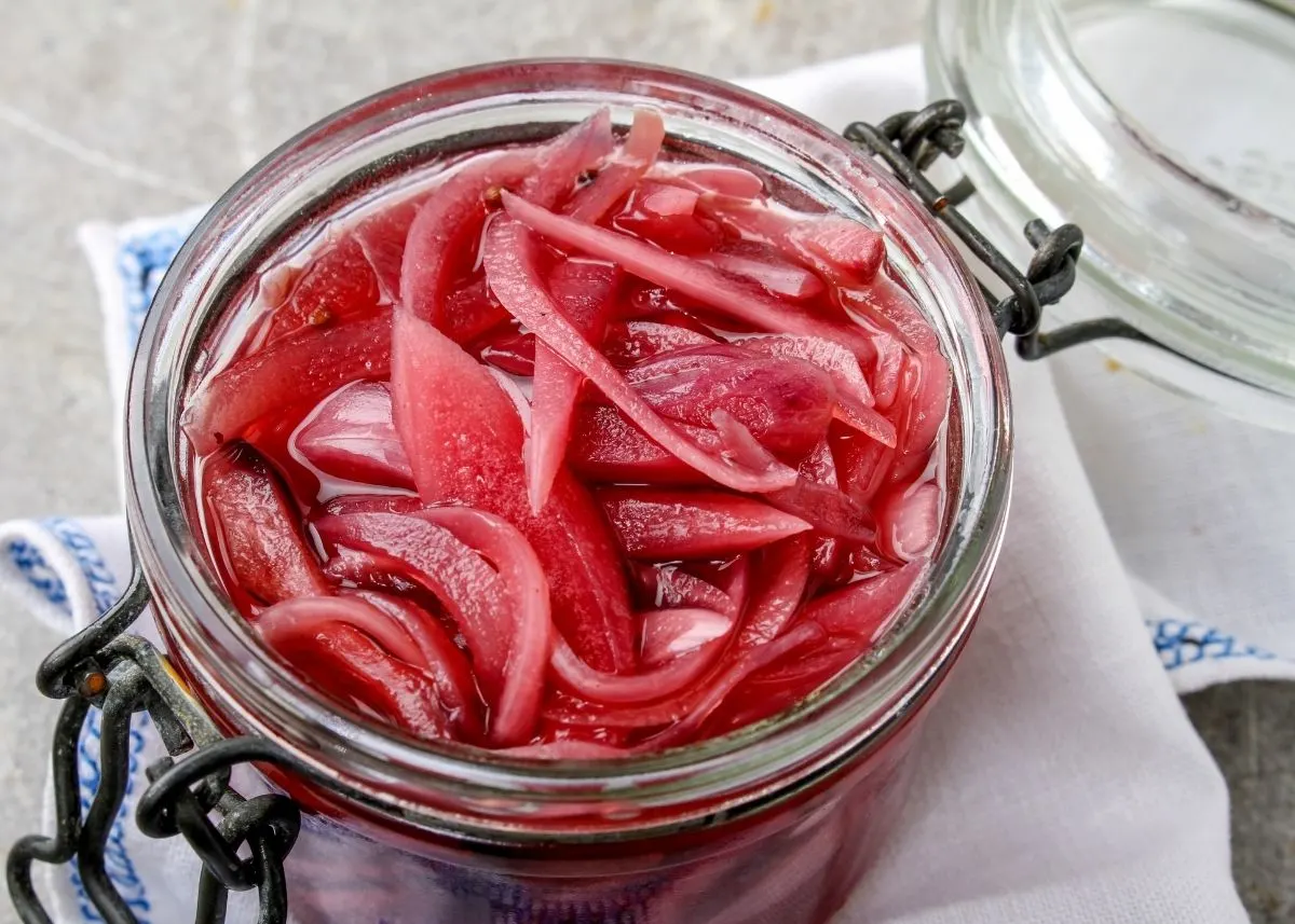 Overhead view of a clear mason jar filled with pickled red onions on tablecloth.
