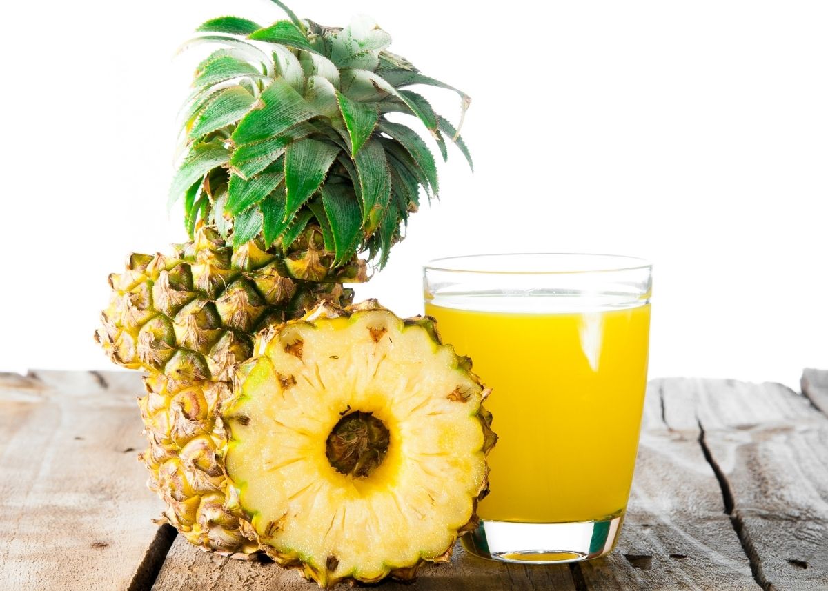 Cut pineapple and slice next to glass of pineapple juice on wooden table.