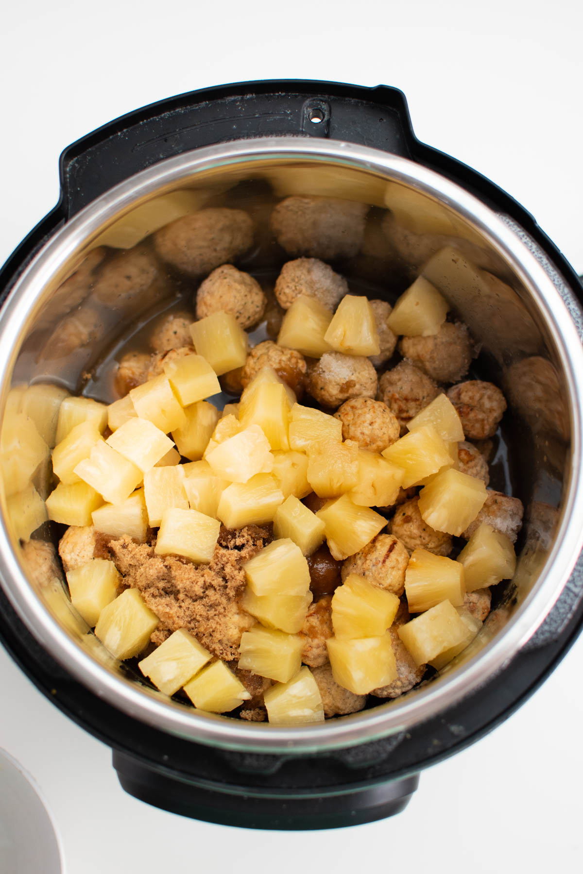Pineapple chunks and frozen meatballs in Instant Pot insert.
