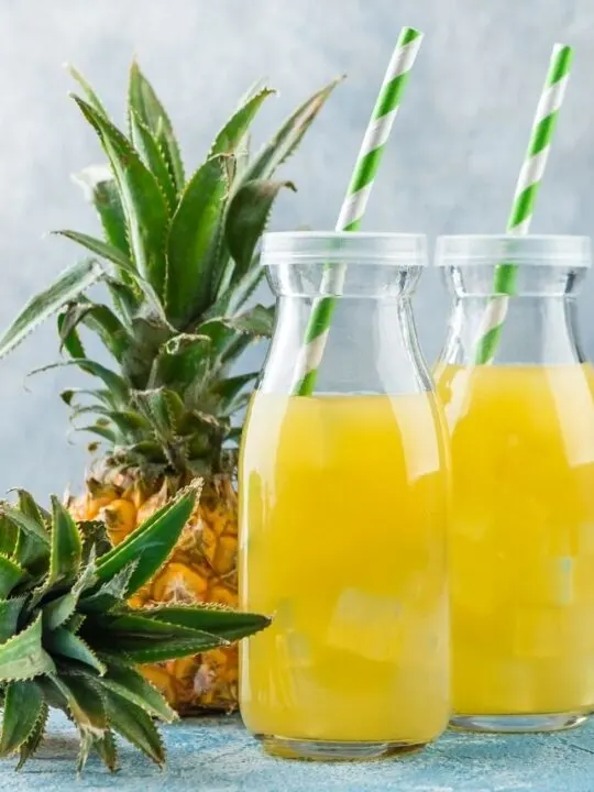 Pineapple juice in two glass jars with straws next to pineapple fruits.