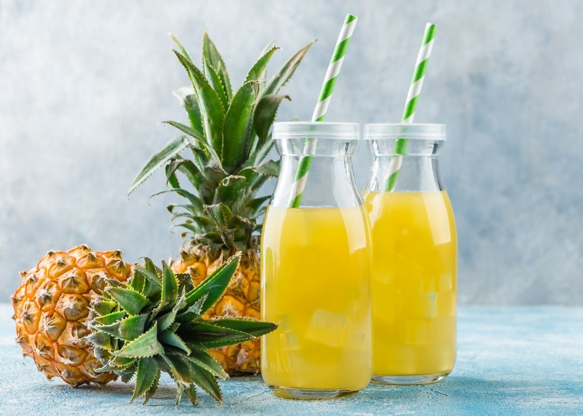 Pineapple juice in two glass jars with straws next to pineapple fruits.