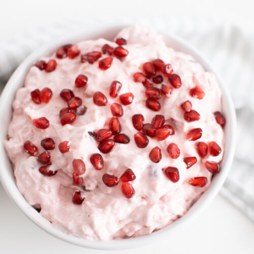 Pink fluff in large white serving bowl with pomegranate arils on top.