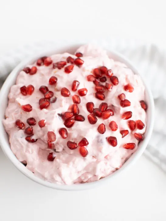 Pink fluff in large white serving bowl with pomegranate arils on top.