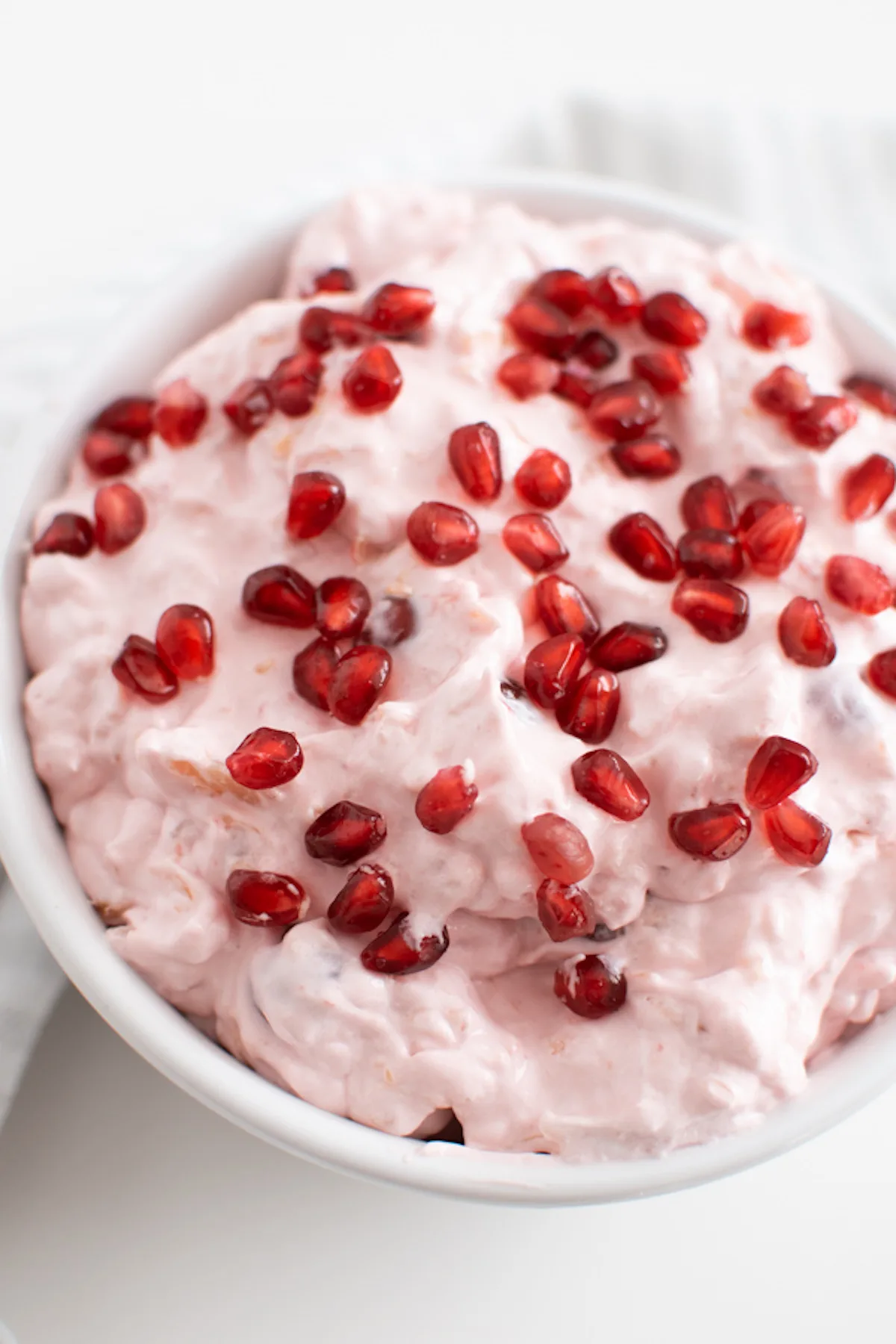 Pink fluff dessert with pomegranate arils on top in white serving bowl.
