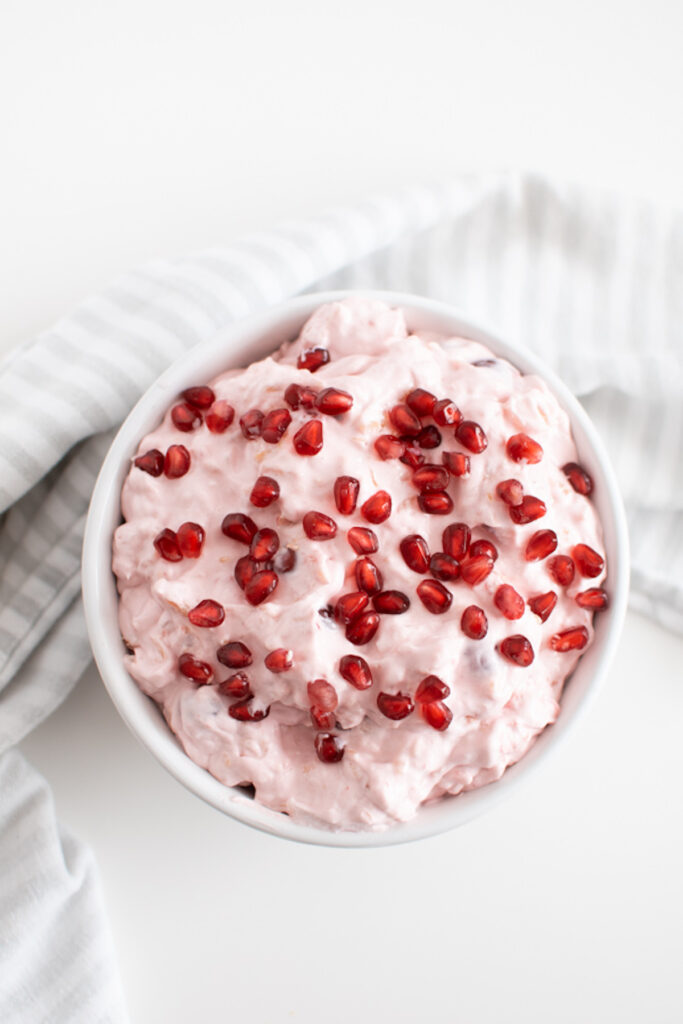 Pink fluff in a white serving bowl topped with pomegranate seeds.