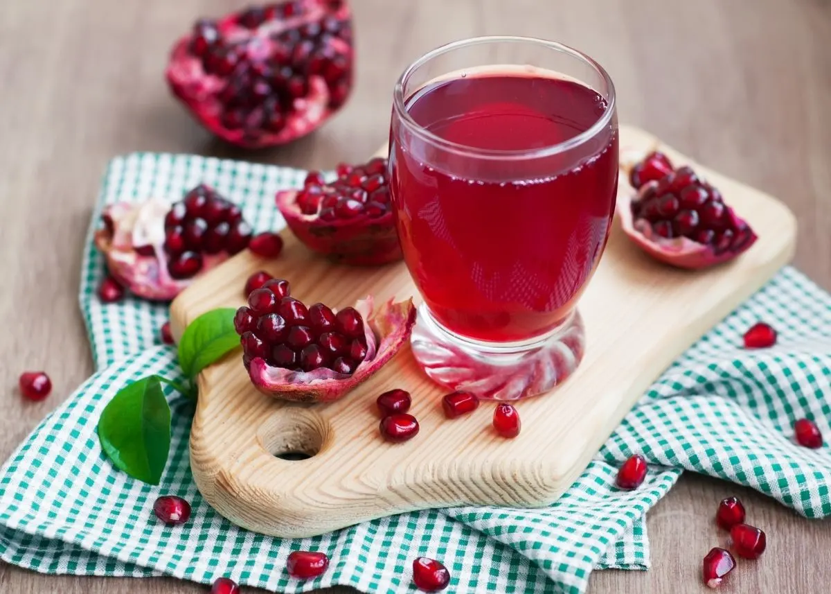 Cut pomegranate fruit scattered around a cutting board and glass of pomegranate juice.