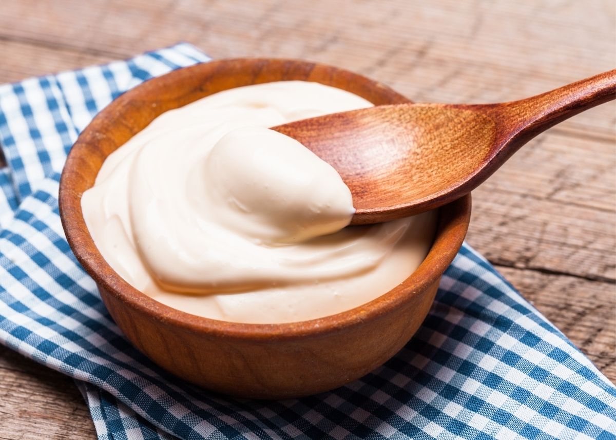 Sour cream in wooden bowl with wooden spoon on white and blue kitchen towel.